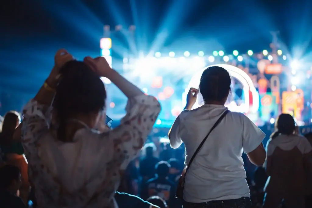 Crowd of hands up concert stage lights and people fan audience silhouette raising hands in the music festival rear view with spotlight glowing effect nightlife event.
